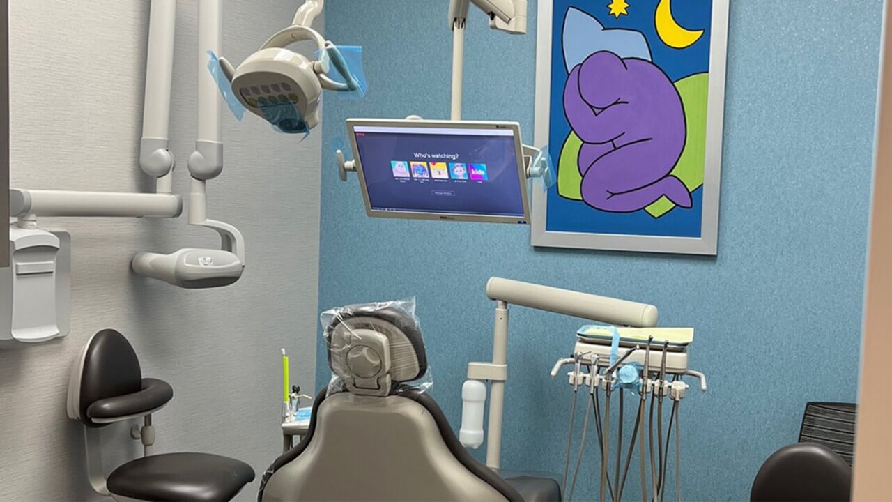 dental exam chair facing a flatscreen TV, art and a blue wall