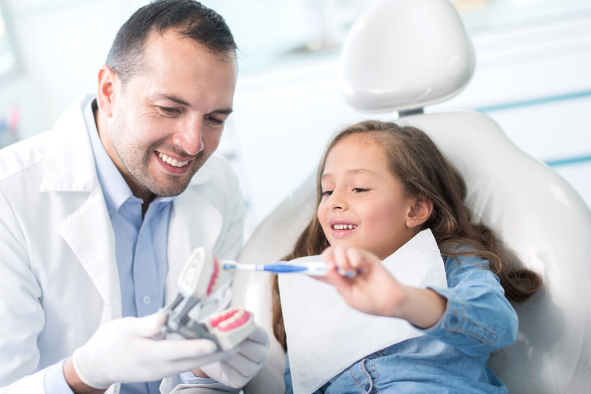 dentist and child practice brushing teeth on a teeth model